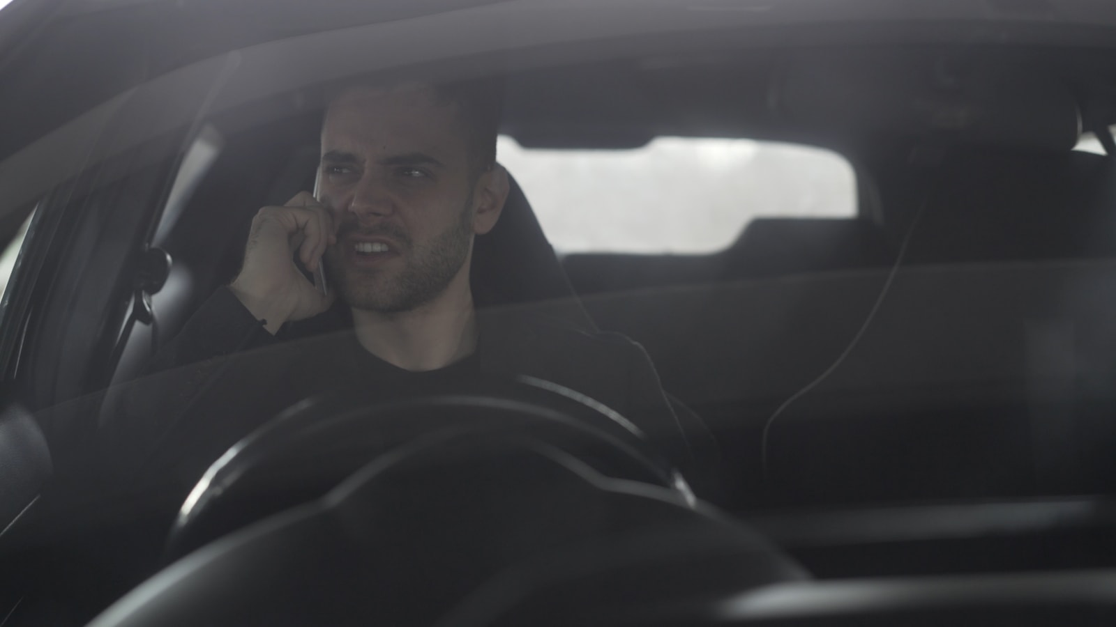 A frustrated person speaking on a phone inside a car